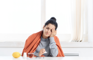 Person resting on a couch with a blanket and a cup of tea, recovering from flu symptoms.