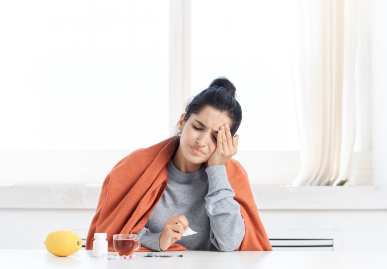 Person resting on a couch with a blanket and a cup of tea, recovering from flu symptoms.