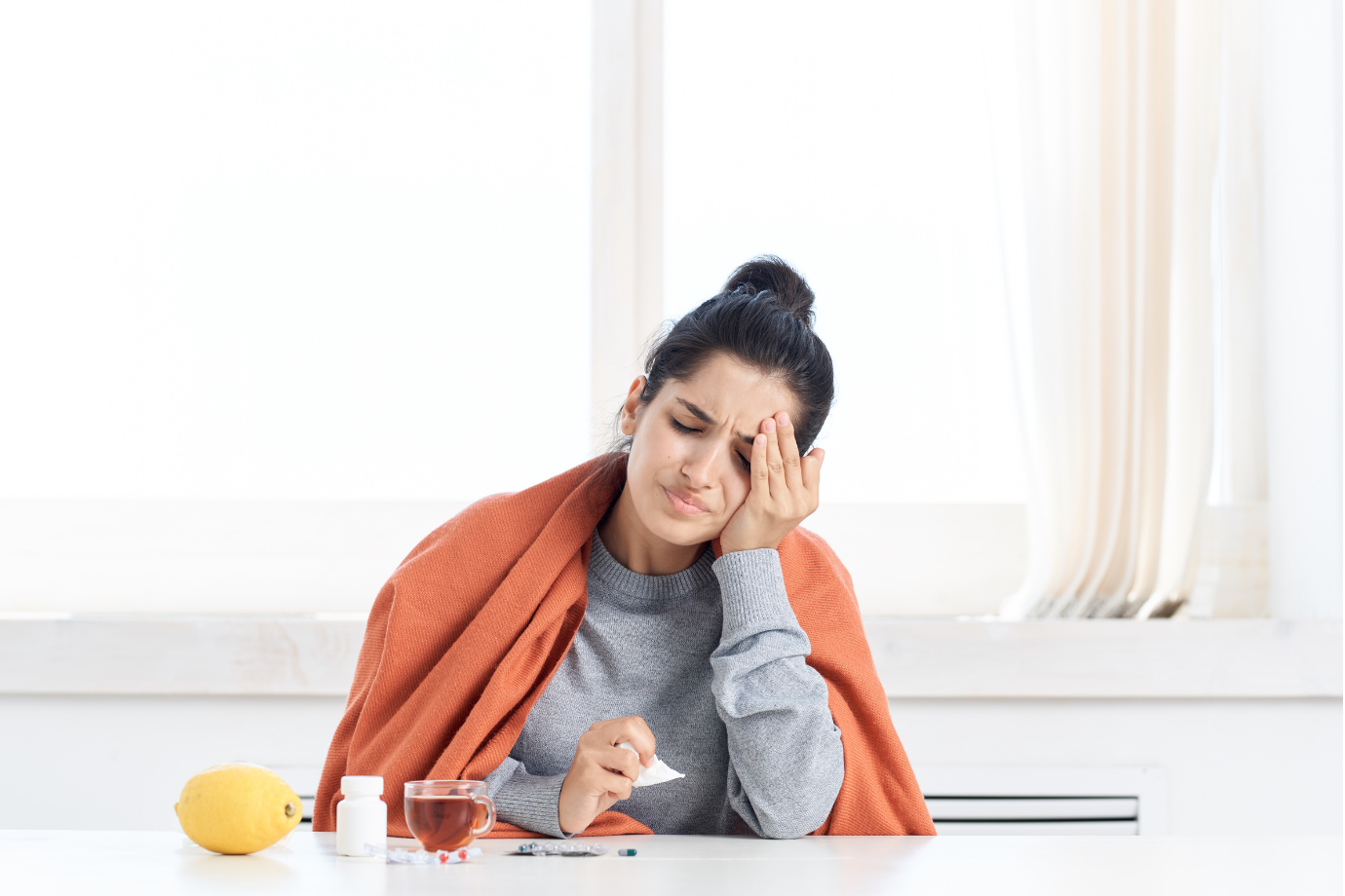 Person resting on a couch with a blanket and a cup of tea, recovering from flu symptoms.